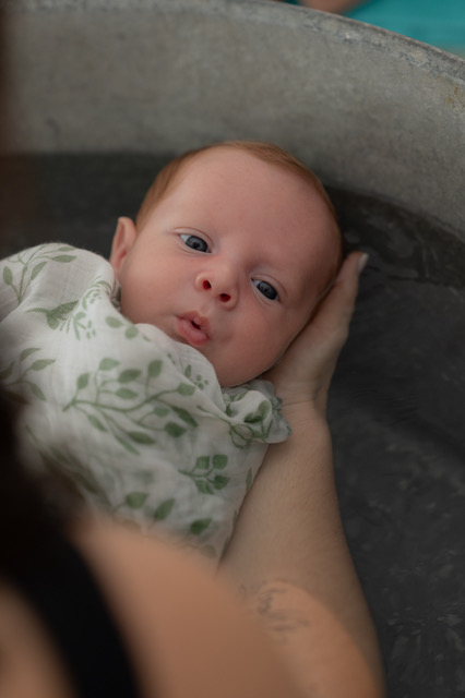 Bébé soutenu dans les bras pendant un bain enveloppé